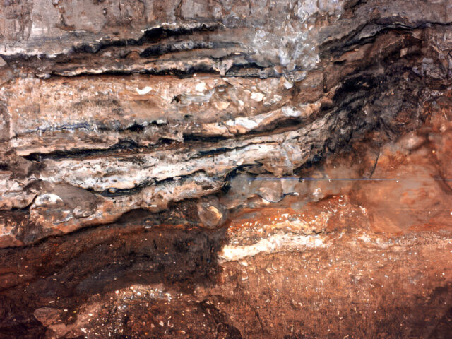 Detail of the stratigraphy inside the cave. Beneath the burned Neolithic grey embankments which are mixed with more recent ones, one can see the hard sediment with corner stones that represents the last Ice Age.